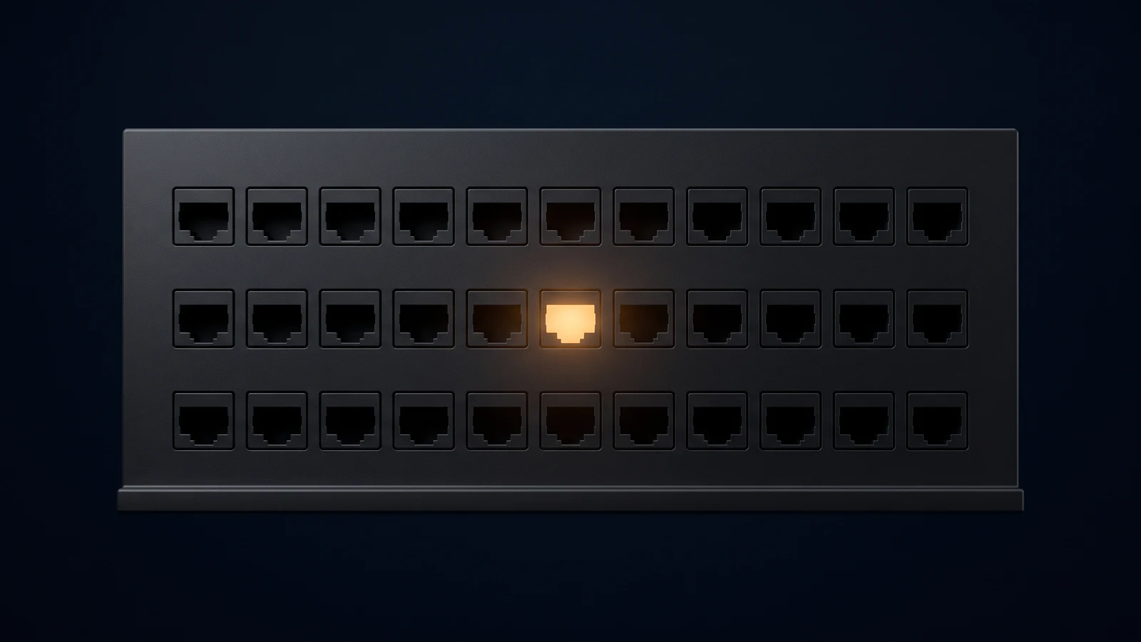 A broad upright connection panel of matte near-black charcoal standing dead-on on a low base rail in a deep blue void, its blank face carrying three long rows of identical empty port recesses all left dark, one single recess in the middle row lit warm amber from deep inside it