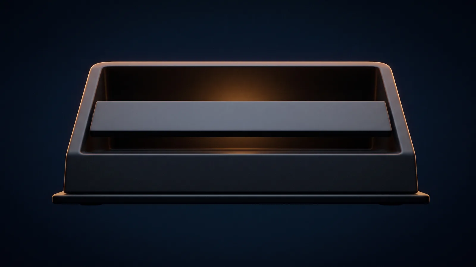 A broad blank dark desktop console resting on a low rail in a deep blue void, one wide unmarked press bar standing proud across the front of its upper face, and the empty recess behind that bar washed warm amber from inside the housing